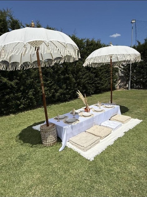 Luxury picnic setup with white parasols and floor cushions on a lawn